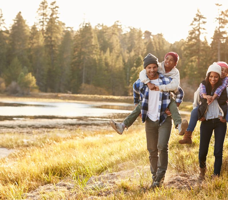 Parents Giving Children Piggyback Ride On Walk By Lake
